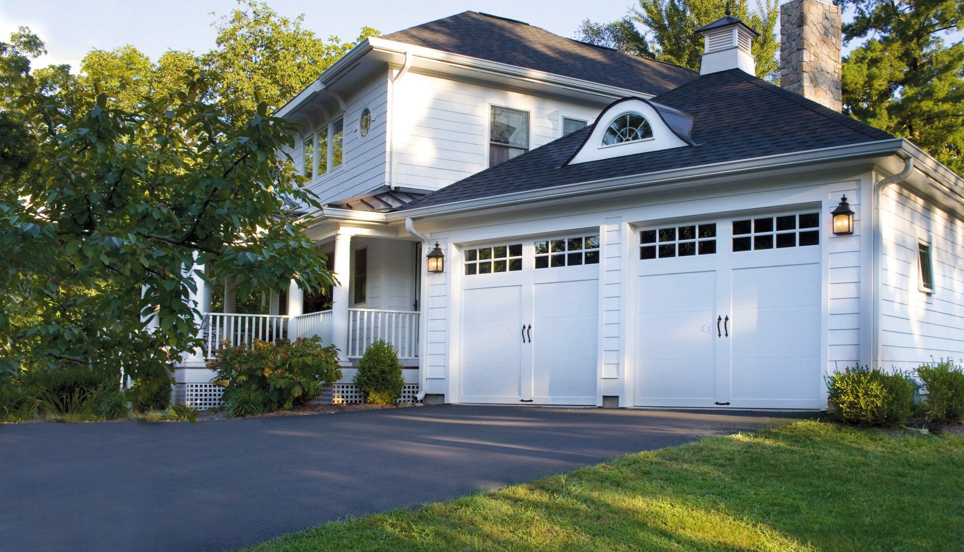 White house with two-car garage, dark asphalt driveway, and green lawn.