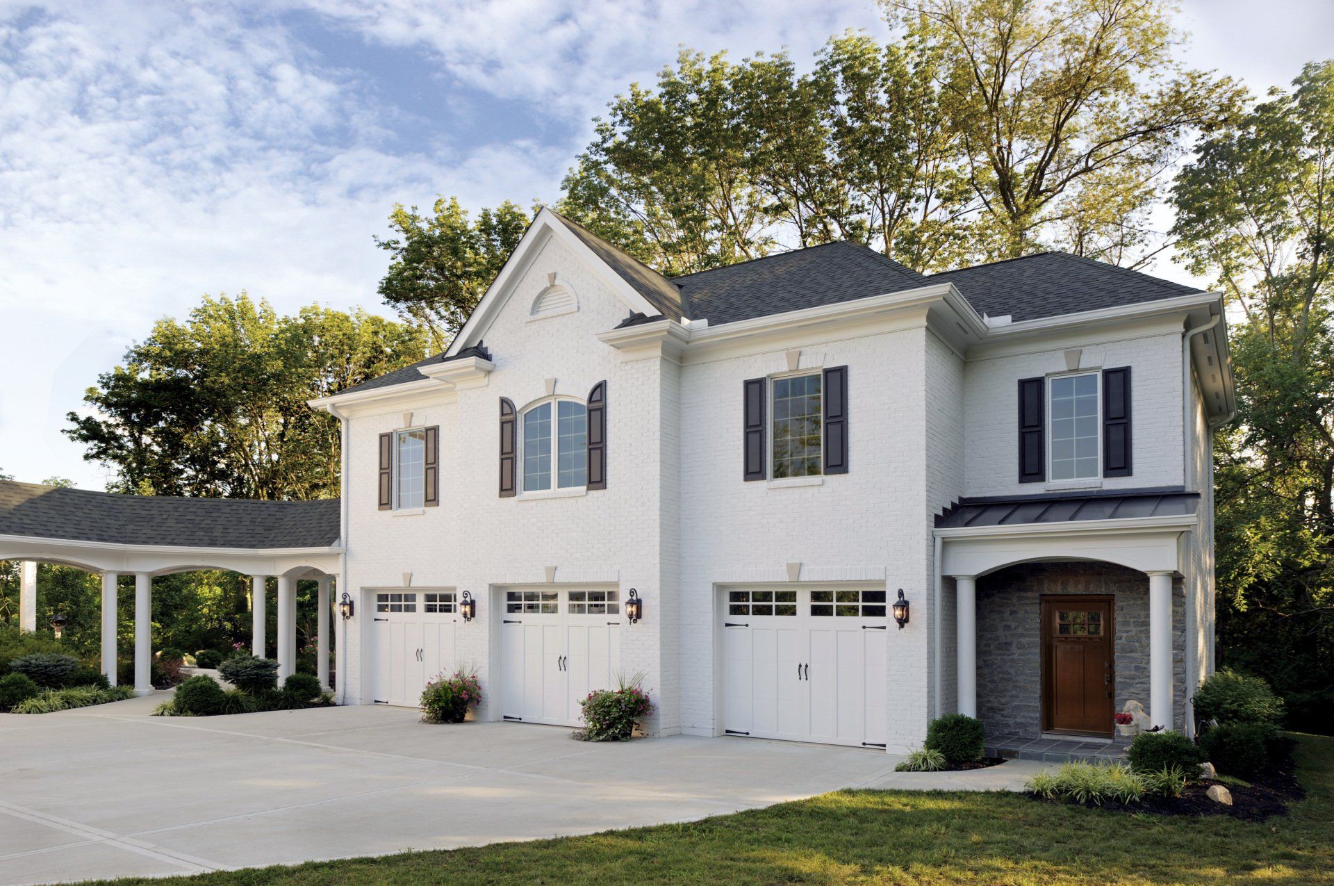 White brick house with three-car garage and carport, black shutters, and brown front door.