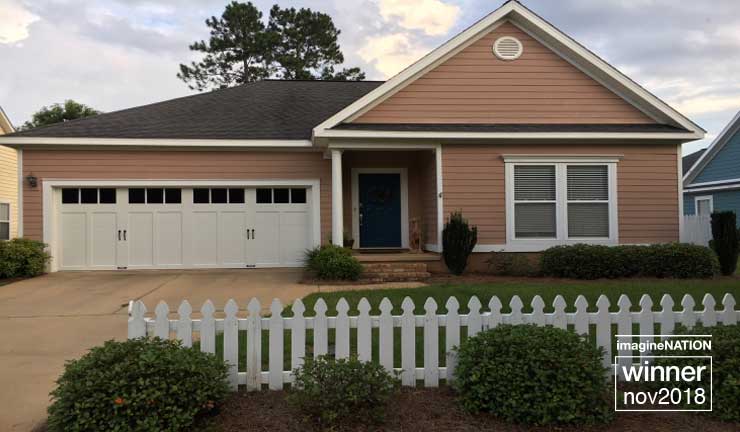 Pink house with white garage and front door, white picket fence, green lawn.