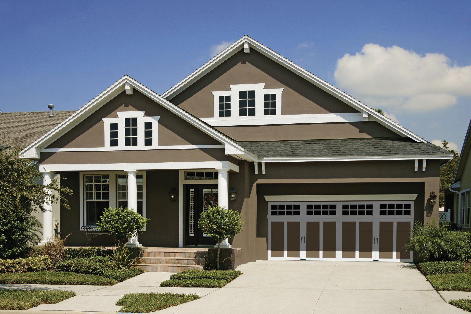 Brown stucco house with white trim, a gabled roof, and a two-car garage.