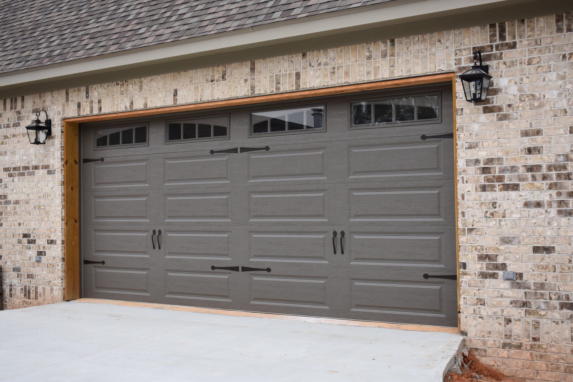 Gray garage door with decorative hardware on a brick building with lights.