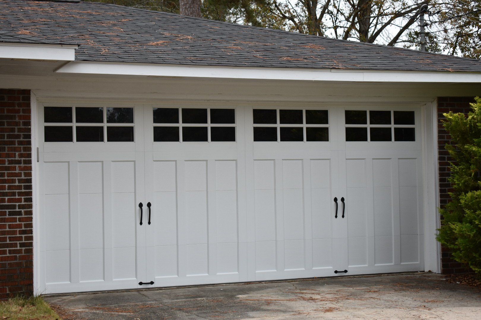 White garage door with rectangular windows, black handles, and brick siding.