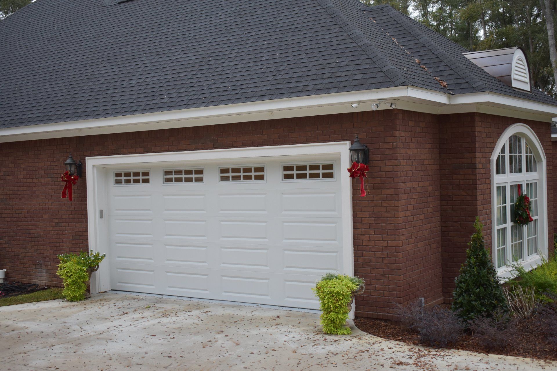 White garage door on brick building with dark roof, decorated with greenery.