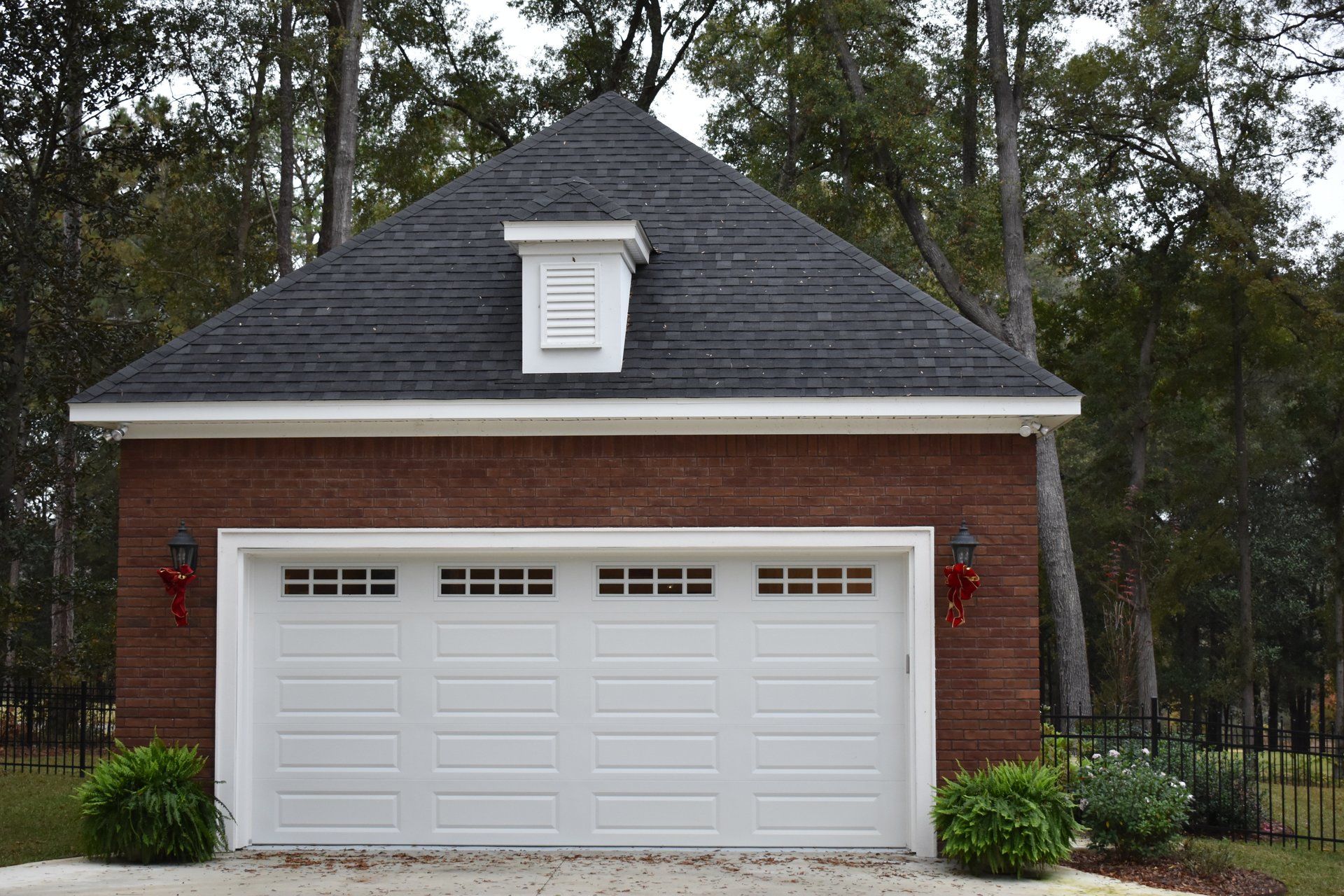 Brick garage with white door and black roof, set in a wooded area.