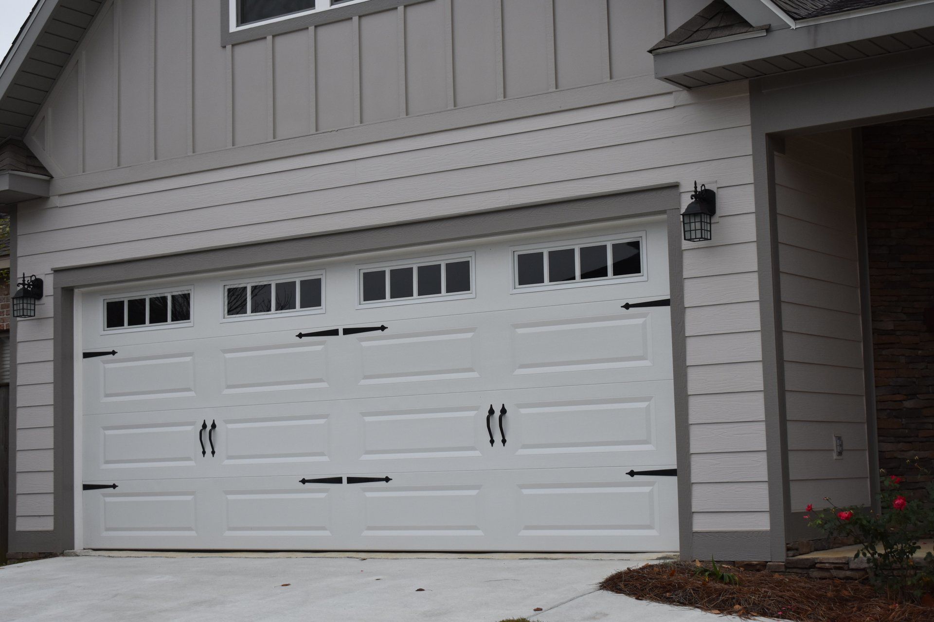 White garage door with decorative hardware and window panels on a gray house.