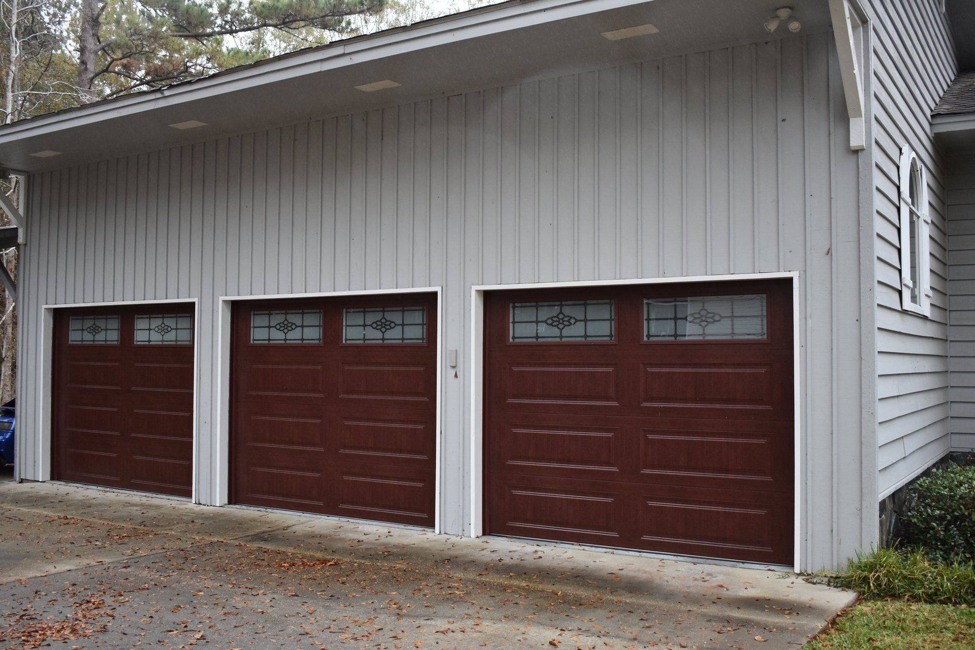 Three-car garage with brown doors and glass windows; light gray siding.
