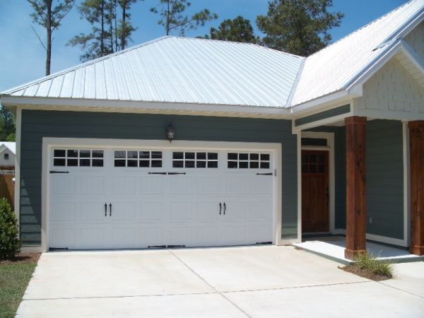 White garage door with windows, teal house exterior, concrete driveway, and white metal roof.