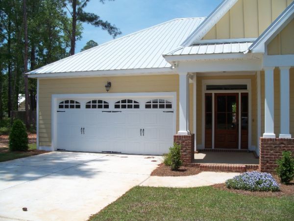 Yellow house with a white garage door, concrete driveway, and covered porch with pillars.