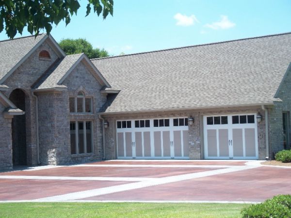 Brick house with two white garage doors and a red driveway on a sunny day.