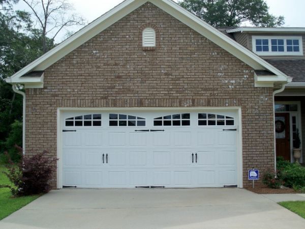 White garage door with windows, on a brick building with a concrete driveway.