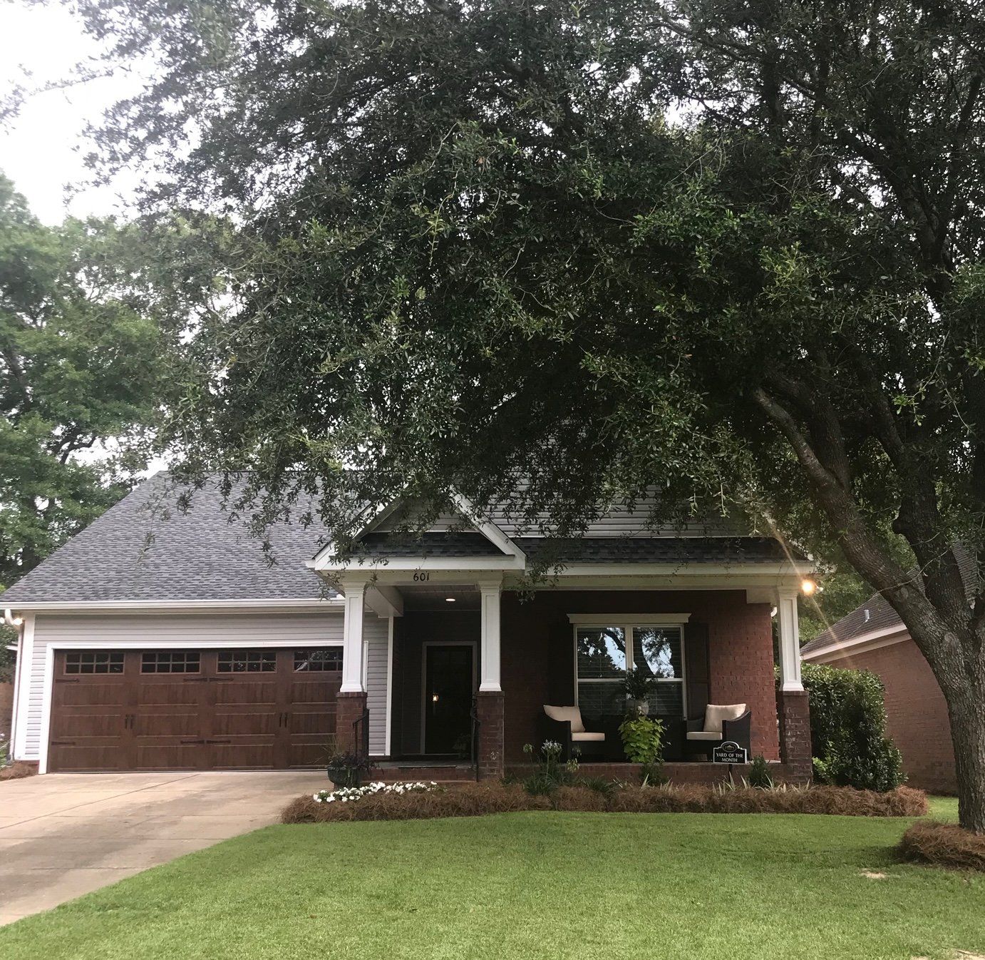 Brick house with a dark brown garage door, front porch, and large tree in the front yard.