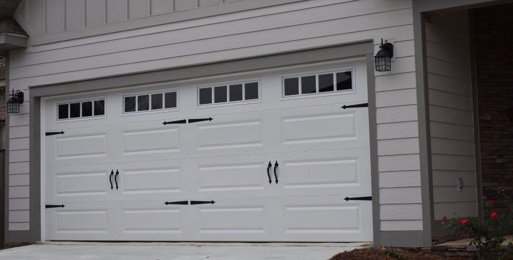 White garage door with decorative black hardware and windows on a house exterior.