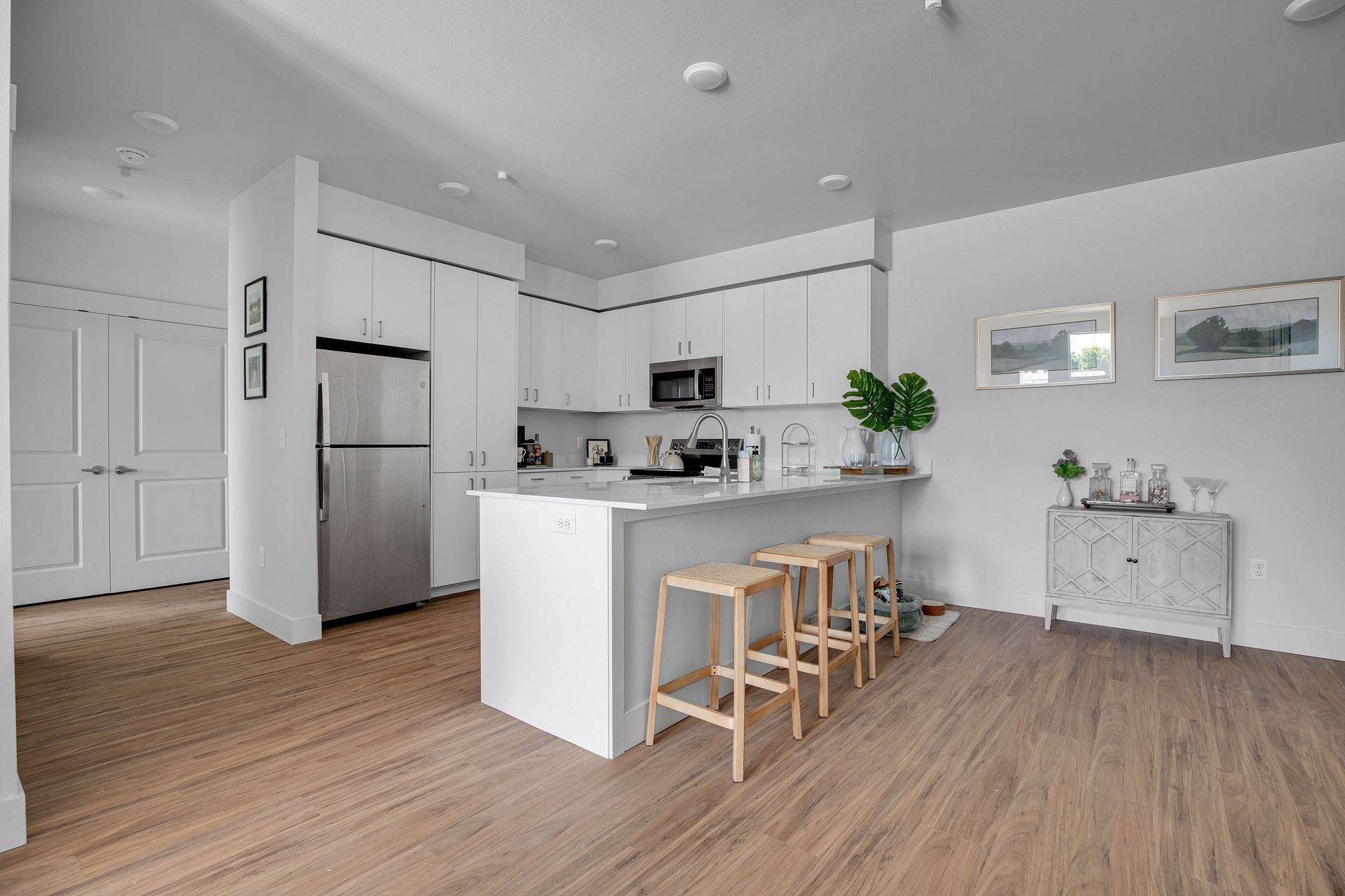 A kitchen with white cabinets , stainless steel appliances , a refrigerator and a bar.