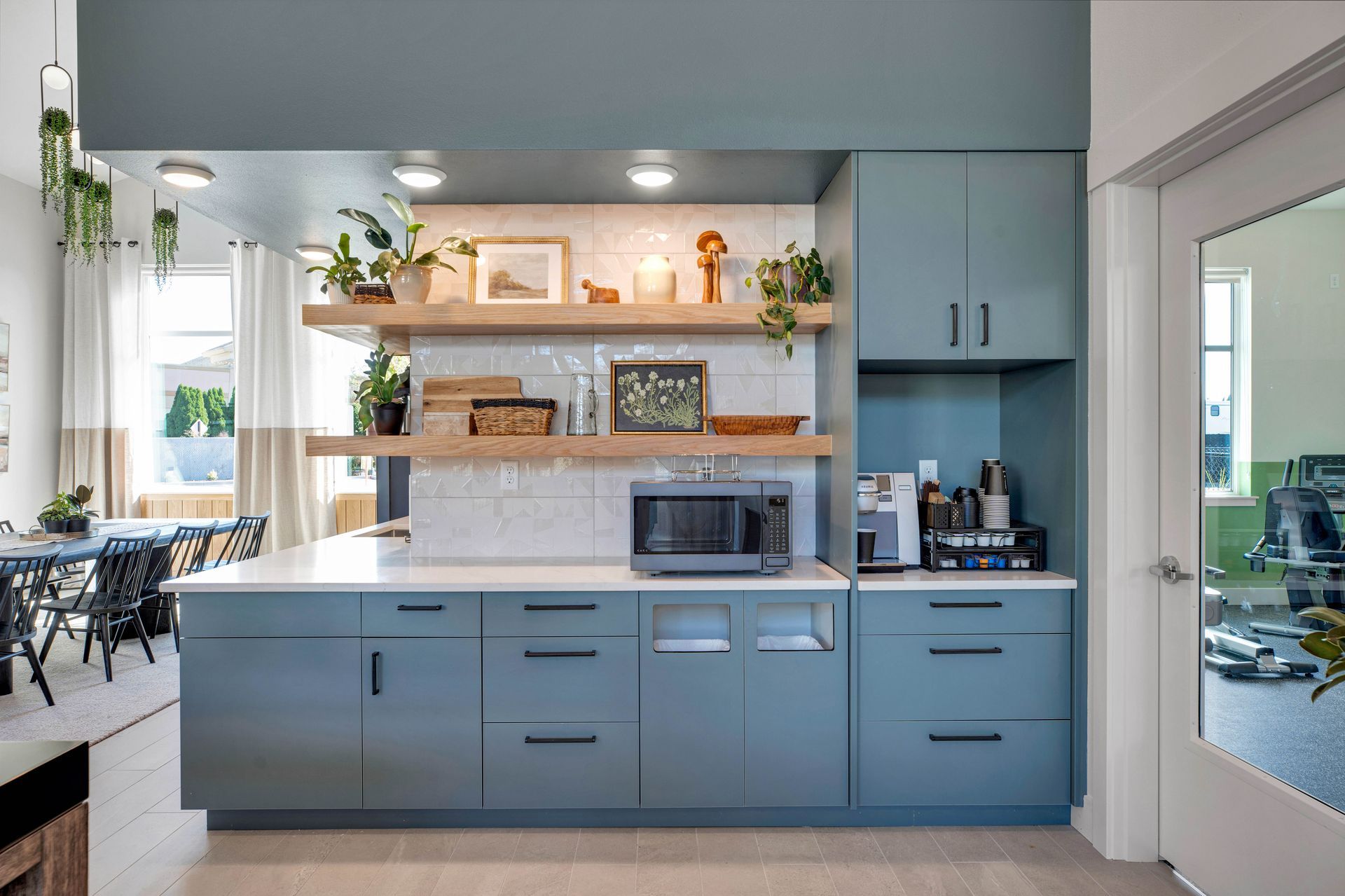 A kitchen with blue cabinets , white counter tops , and a microwave.