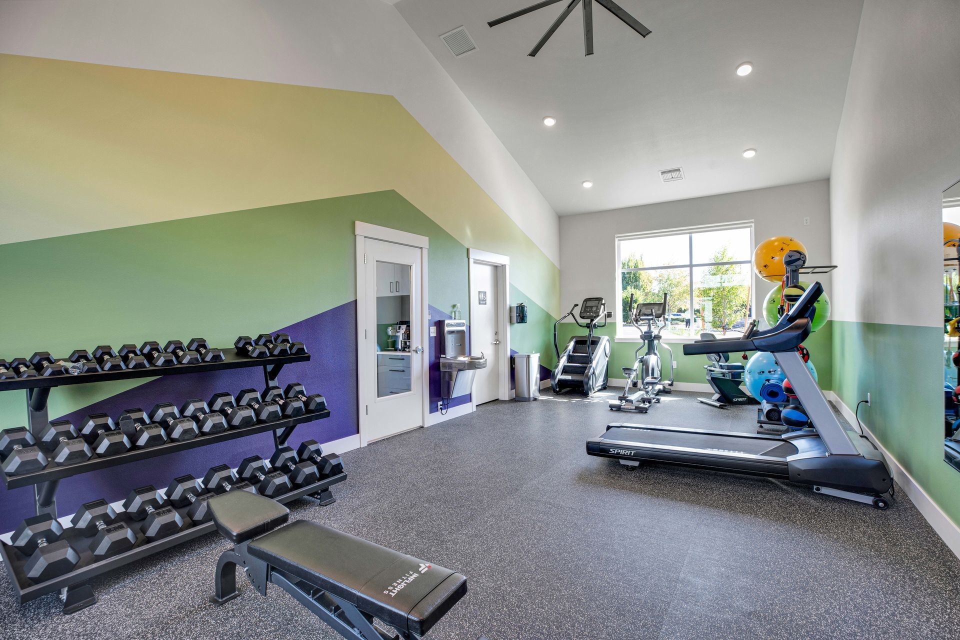 A gym with a treadmill , dumbbells , and a bench.