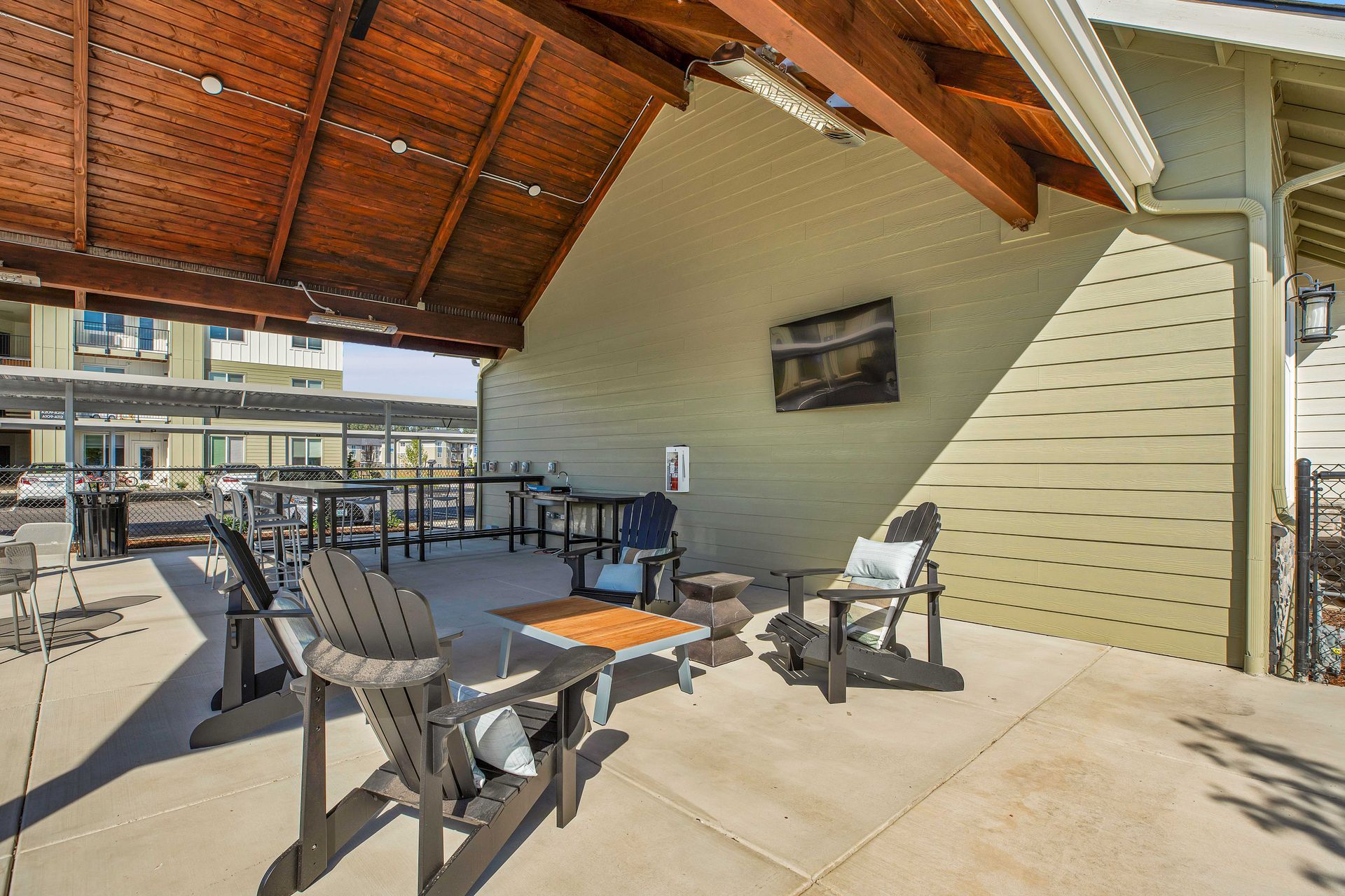 A patio with chairs and tables under a wooden roof.