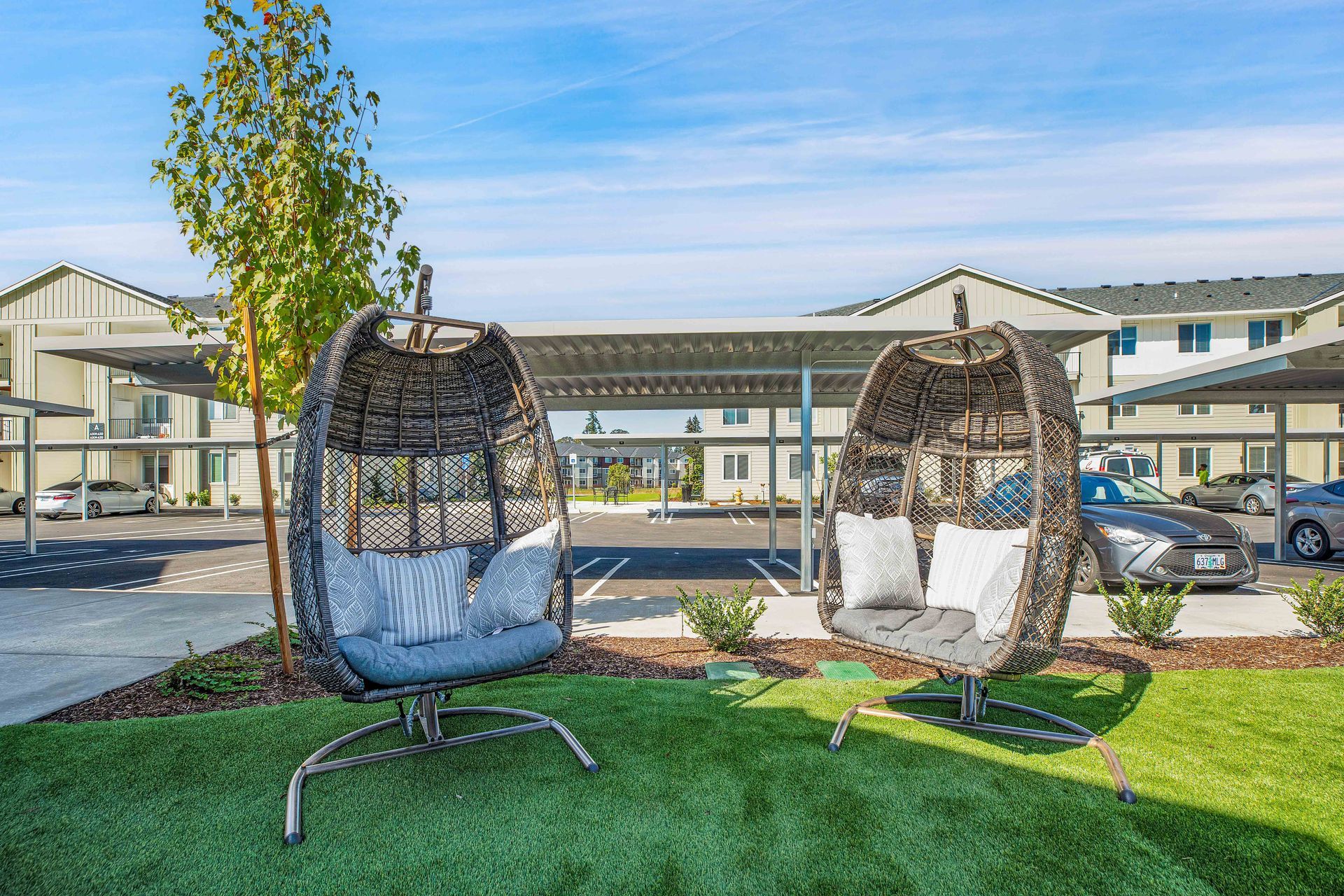 Two wicker chairs are sitting on top of a lush green lawn in front of a building.