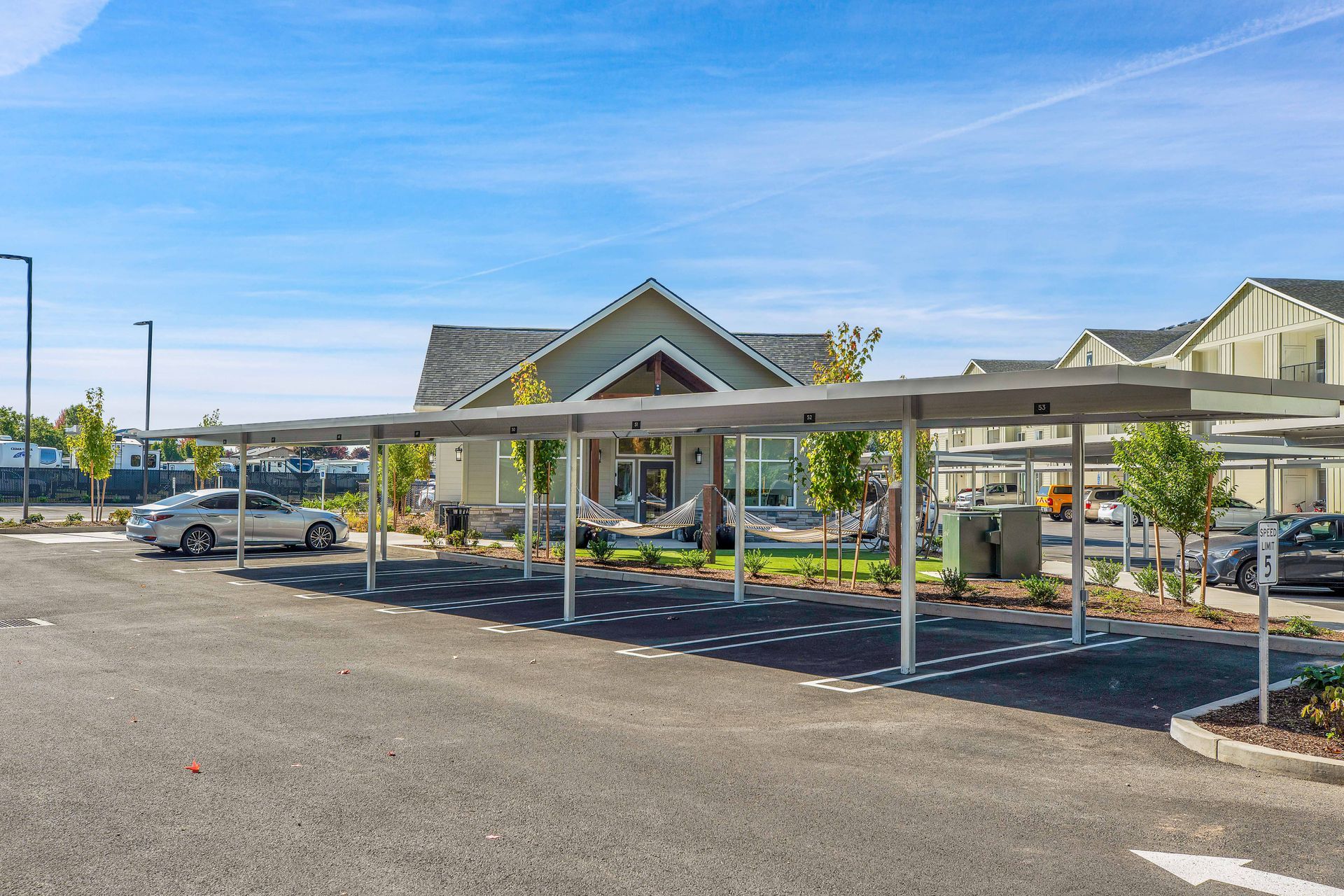 A parking lot with cars parked under a canopy in front of a house.