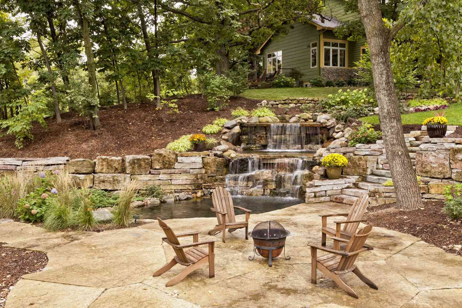A patio with chairs and a fire pit in front of a waterfall.