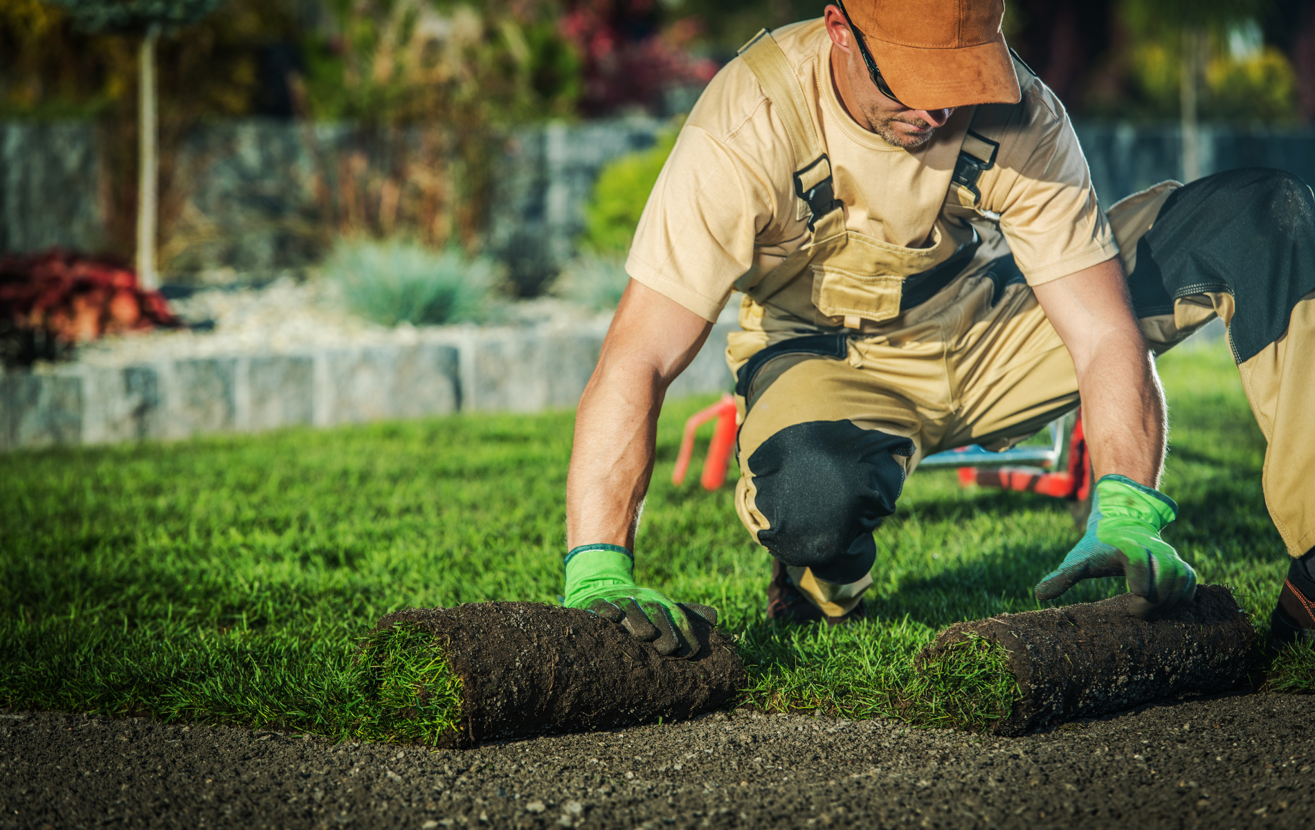 A man is kneeling down and rolling a roll of grass on the ground.