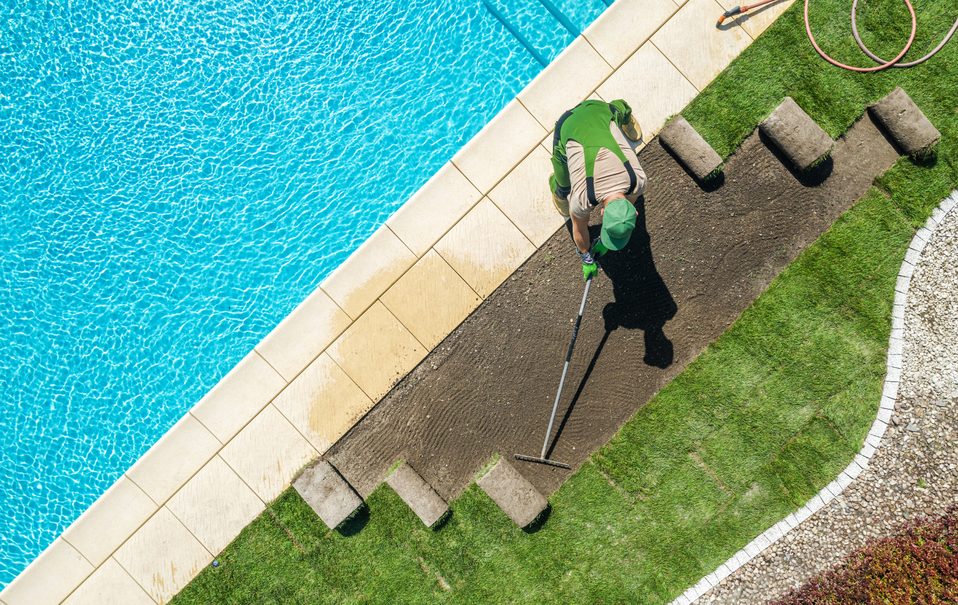 A man is raking the grass next to a swimming pool.