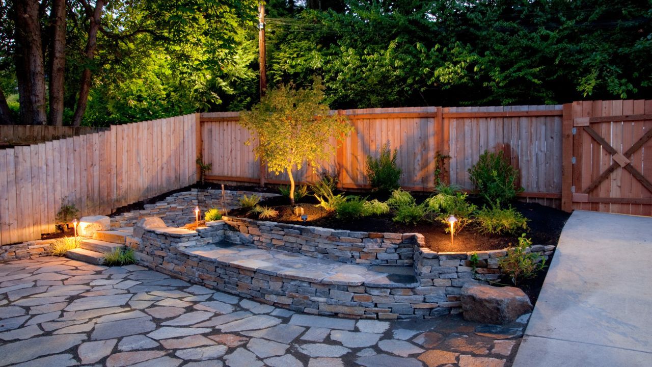 A backyard with a stone wall and a wooden fence at night.