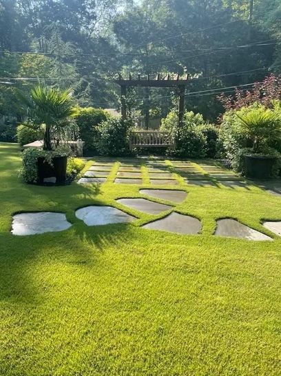 A lush green lawn with stone walkways and a pergola in the background.