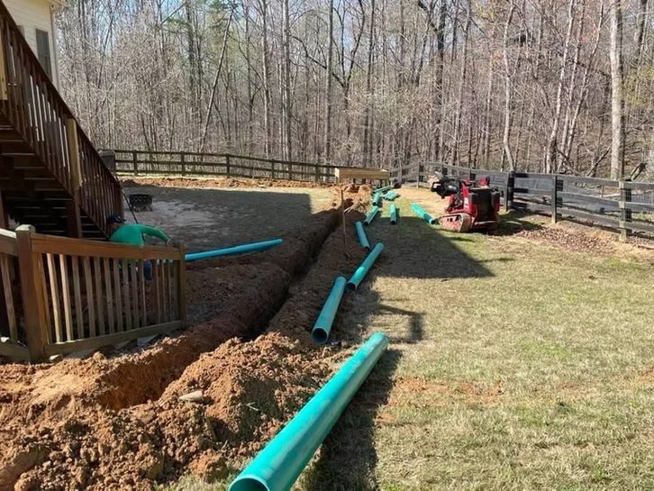A bunch of green pipes are laying in the dirt in front of a house.