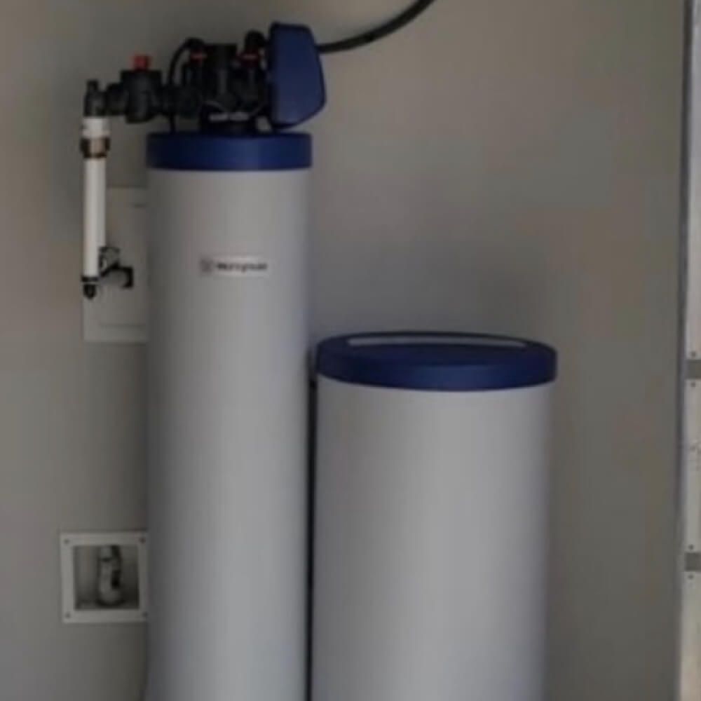 A water softener is sitting next to a water tank in a room.
