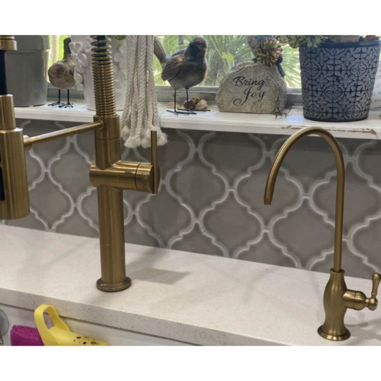 A kitchen sink with a brass faucet and a sign that says bring joy