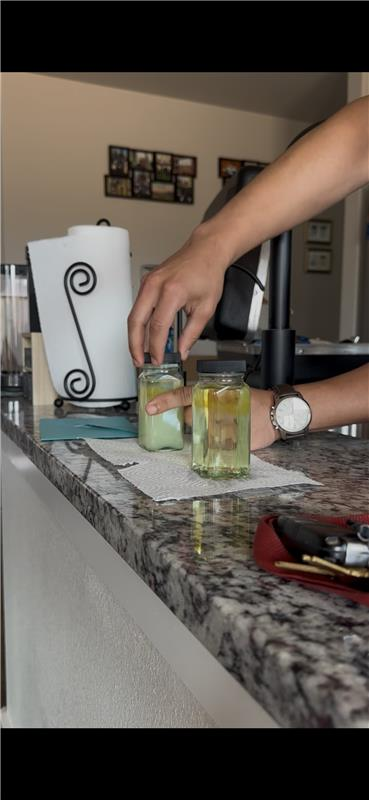 A person arranging jars on a countertop, near a paper towel holder.