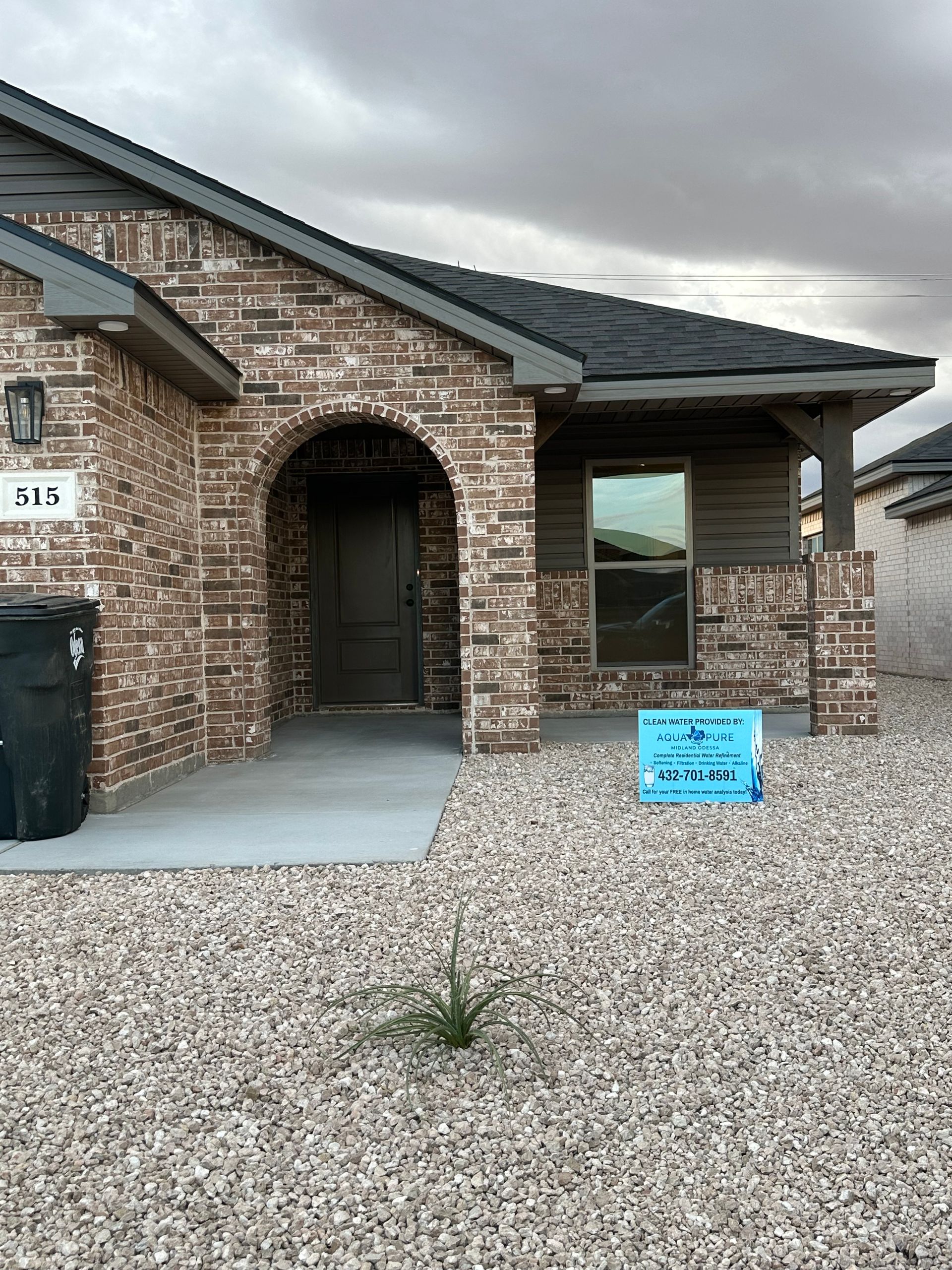 Brick house with arched doorway, black door, gray gravel, blue sign.