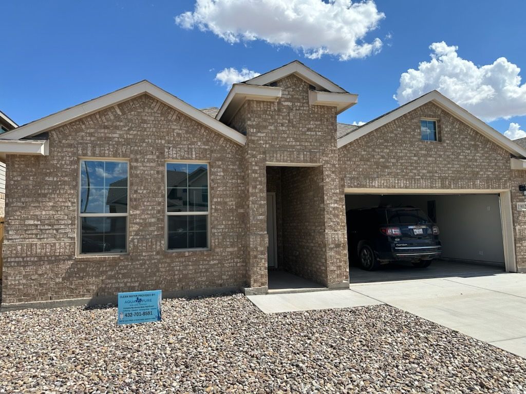 Brick house with a two-car garage. A dark car is parked inside. Blue sky.