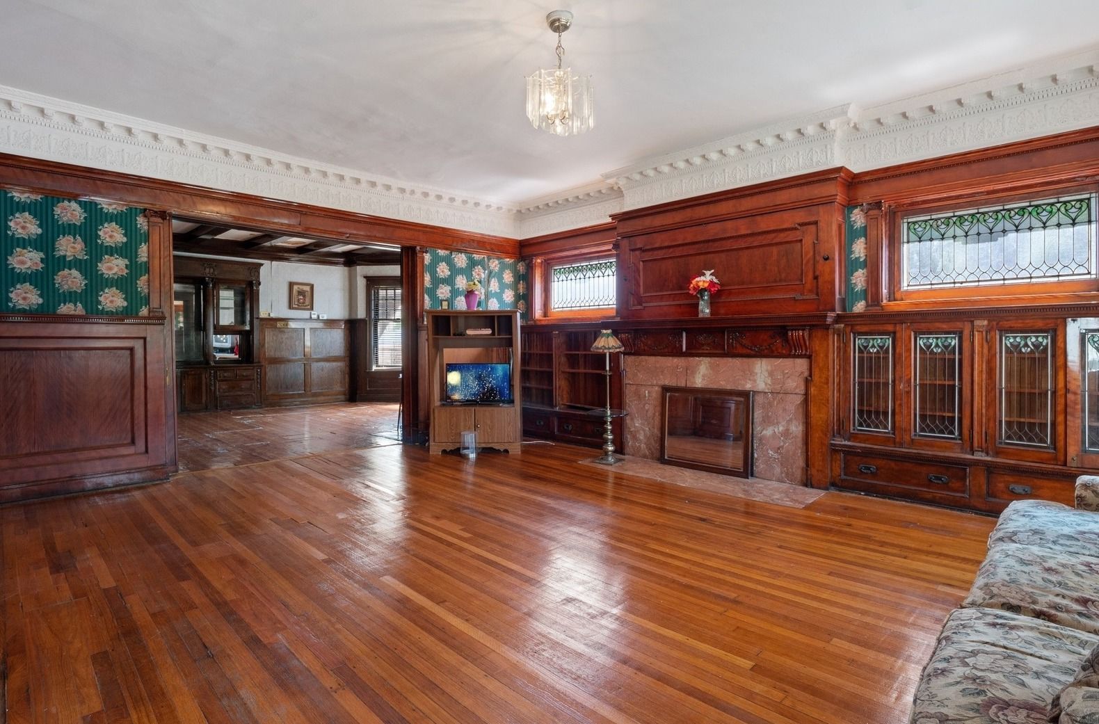 Empty wood-paneled living room with polished hardwood floors, fireplace, and patterned wallpaper