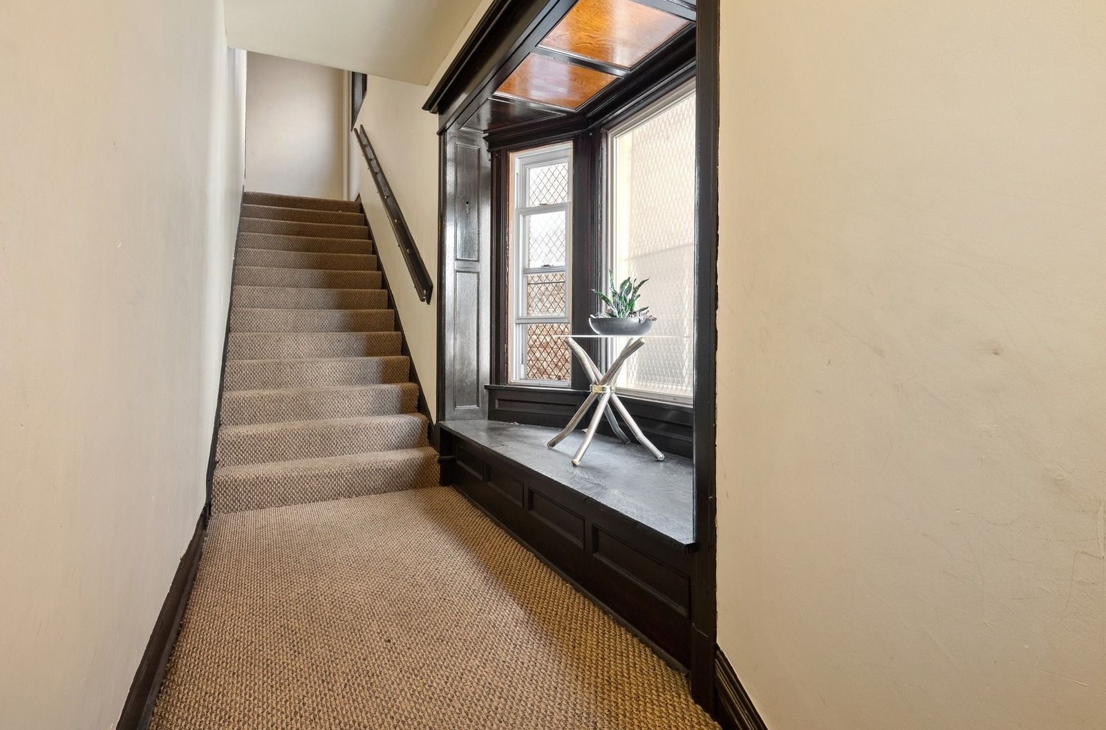 Carpeted stairwell beside a dark-framed window seat with a small table and plant
