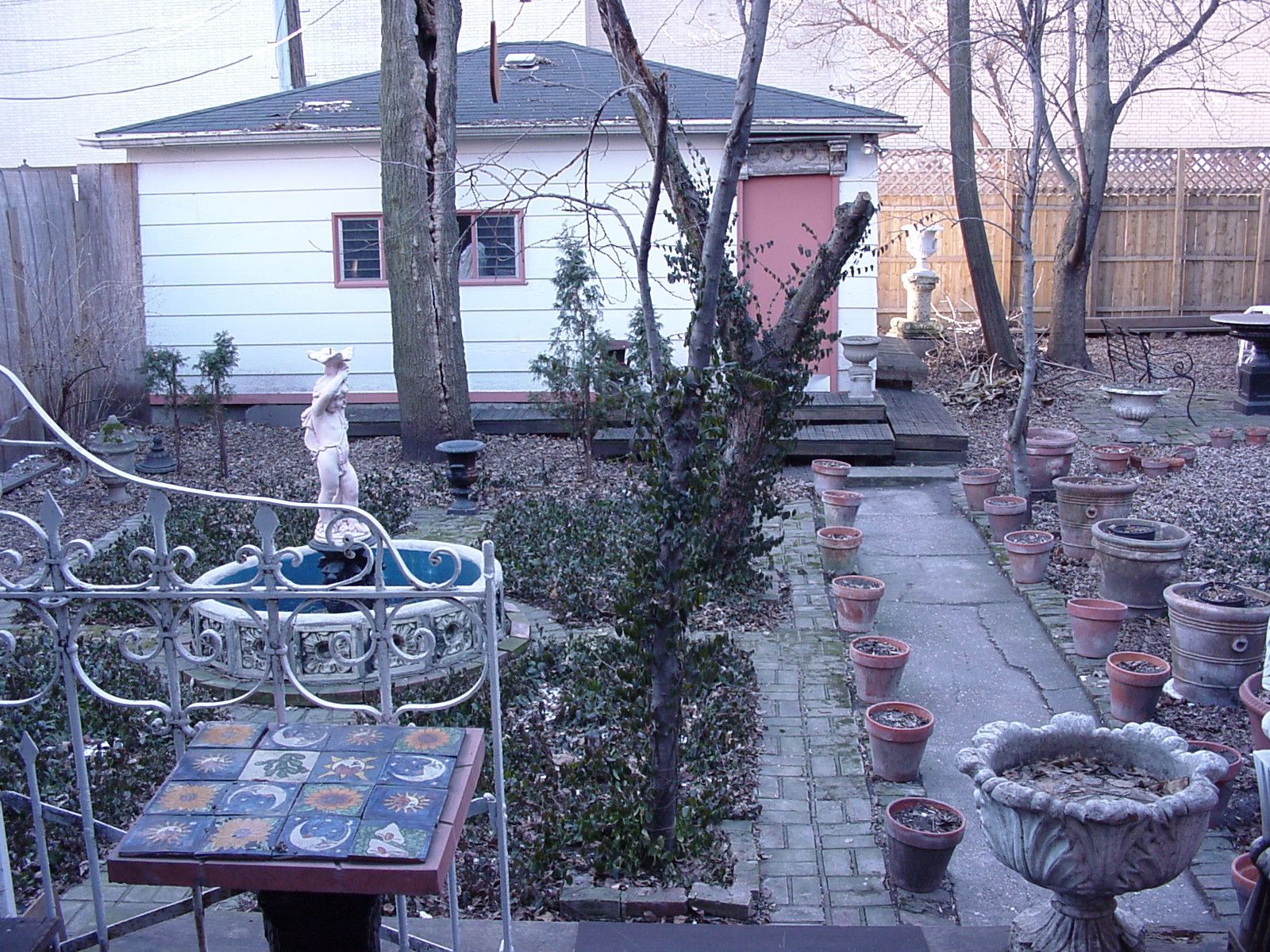 Backyard garden with potted plants, a white shed, stone path, and a decorative fountain.