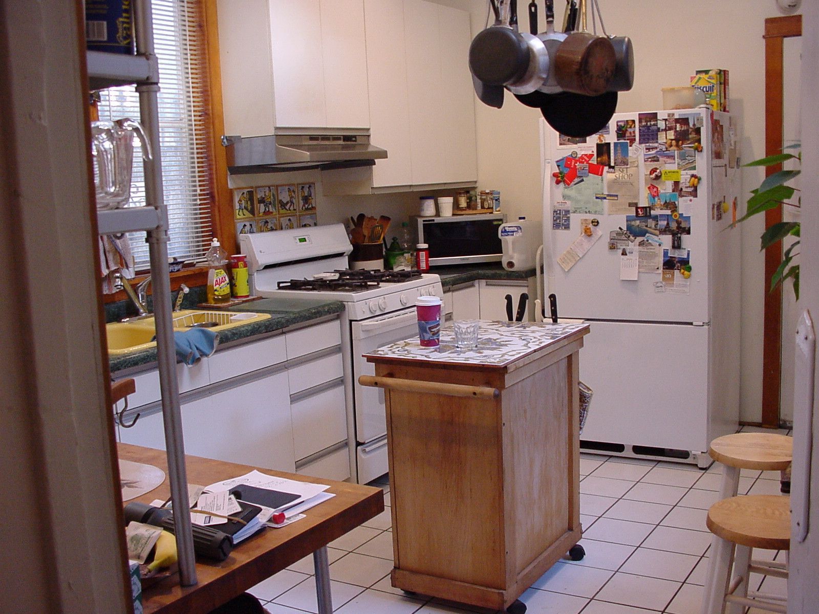 Small kitchen with white cabinets, hanging pots, a fridge covered in magnets, and a central island.