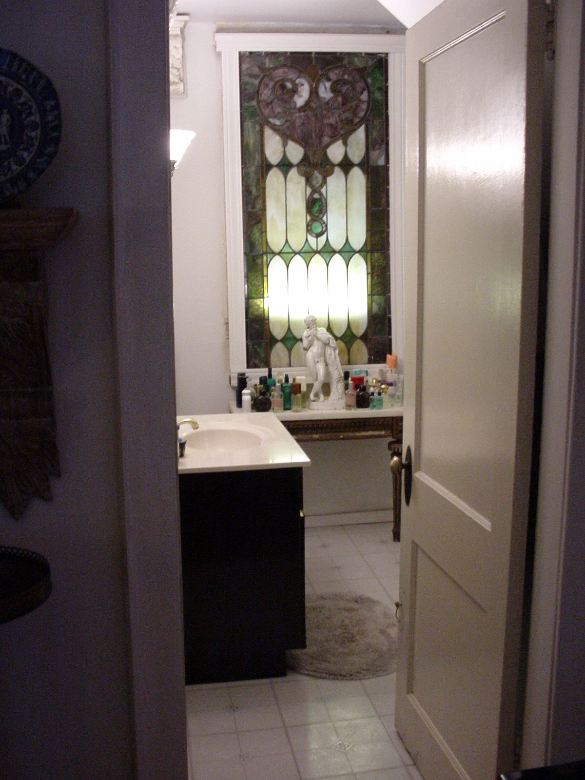 Narrow bathroom hallway with a sink, dark vanity, and stained-glass window at the far end.