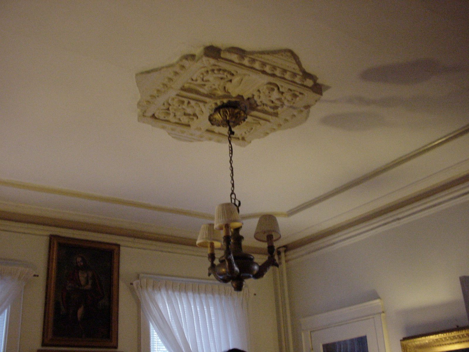 Ceiling light fixture with ornate floral medallion in a room with crown molding and a window below