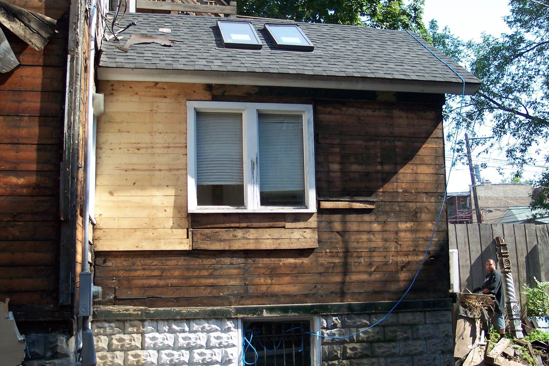 Weathered wooden house exterior with a white-framed window and two skylights on a shingled roof