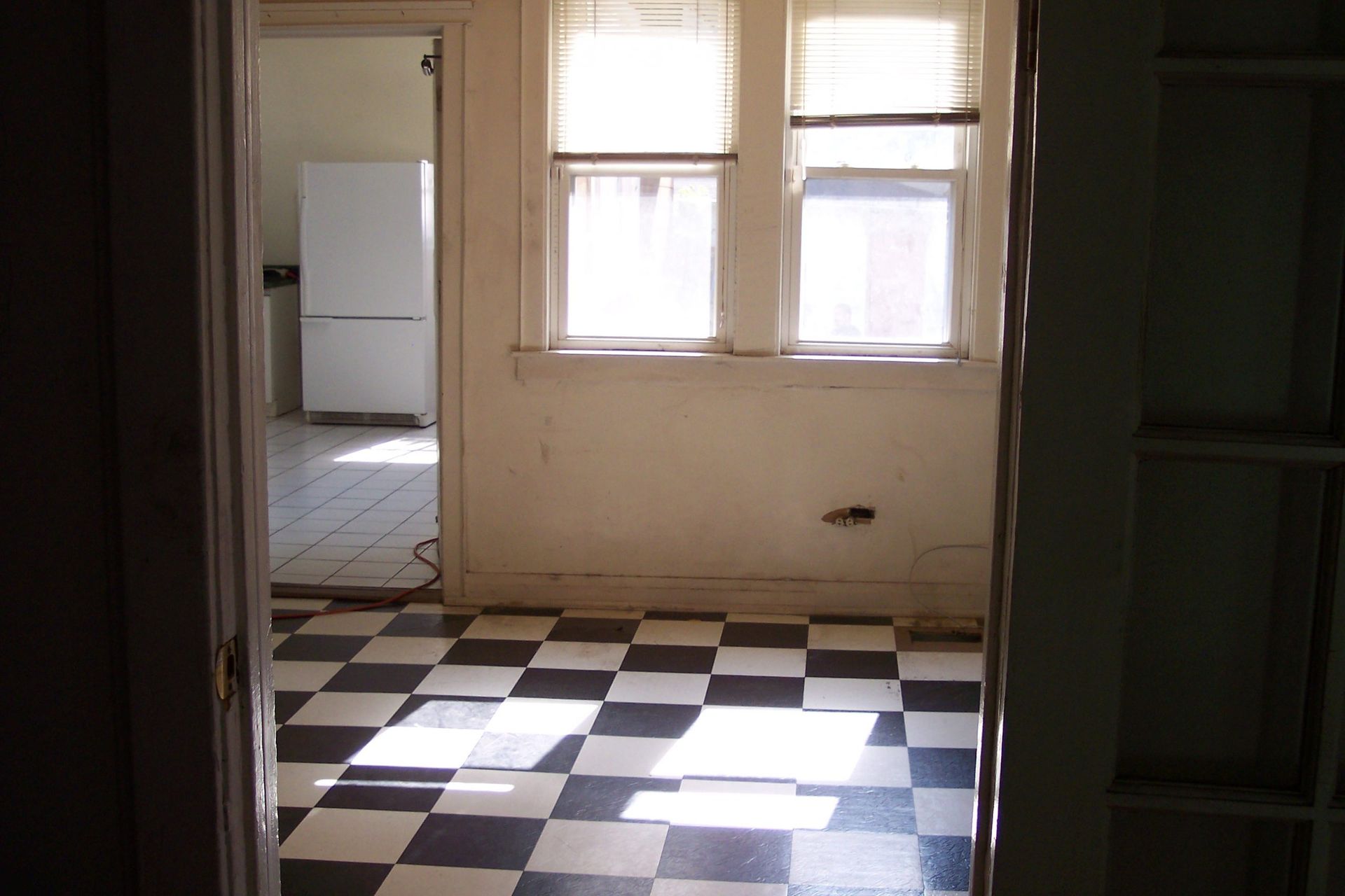 Empty kitchen with black-and-white checkered floor and two windows.