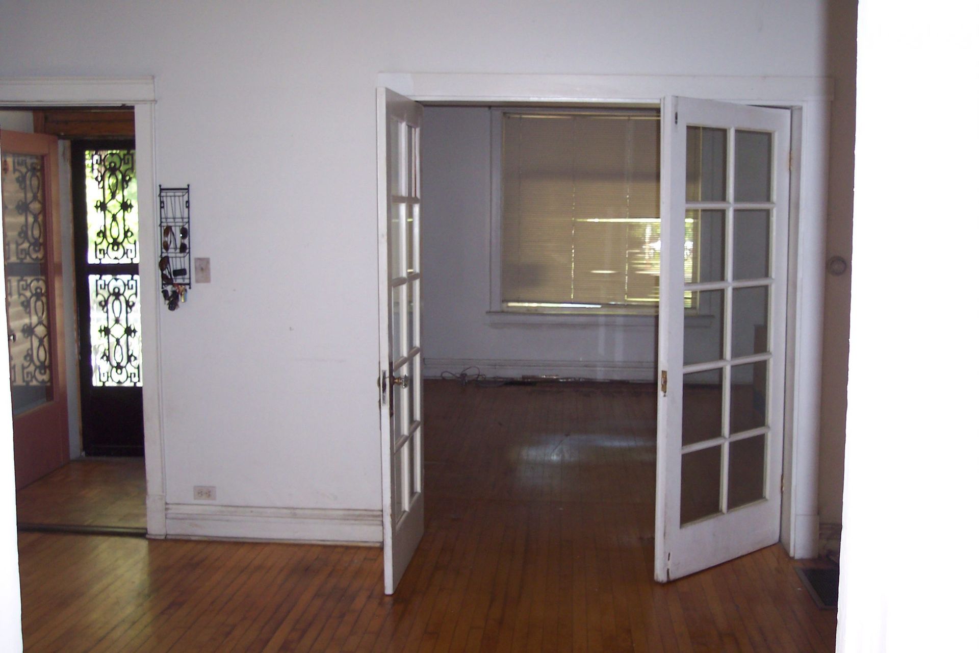 Empty room with hardwood floors and French doors leading to a larger room.