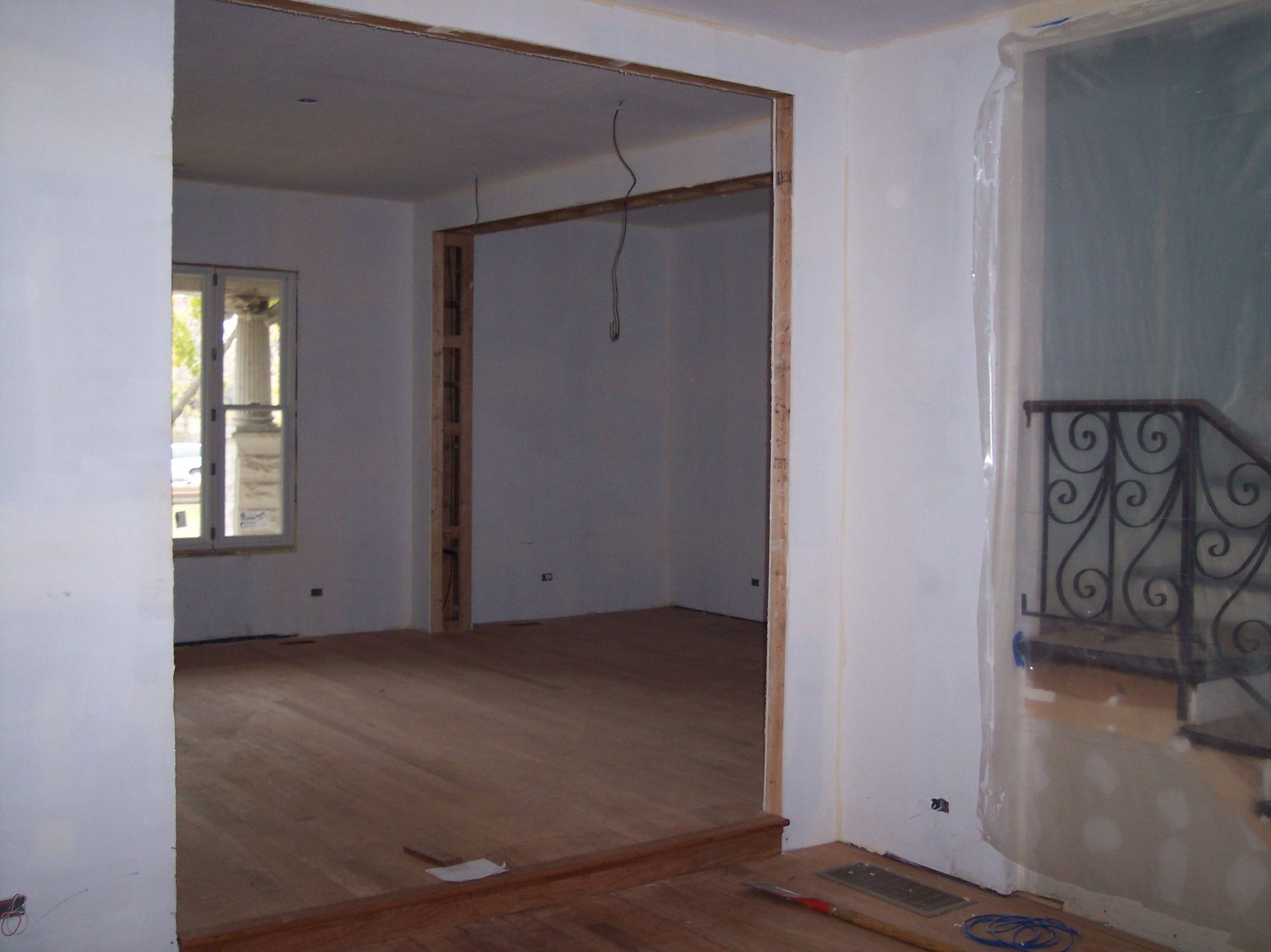 Empty room with white walls, wood floor, and a window near a decorative metal railing.