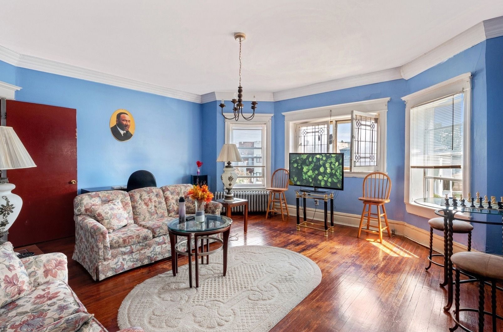 Bright blue living room with floral sofa, hardwood floors, TV, and large windows