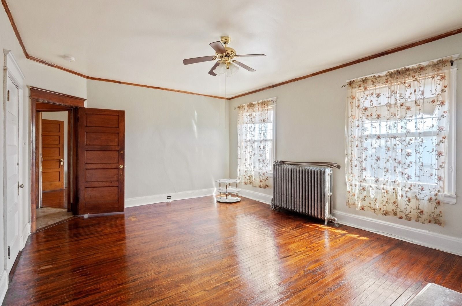 Empty room with hardwood floors, white walls, two windows, and a ceiling fan.