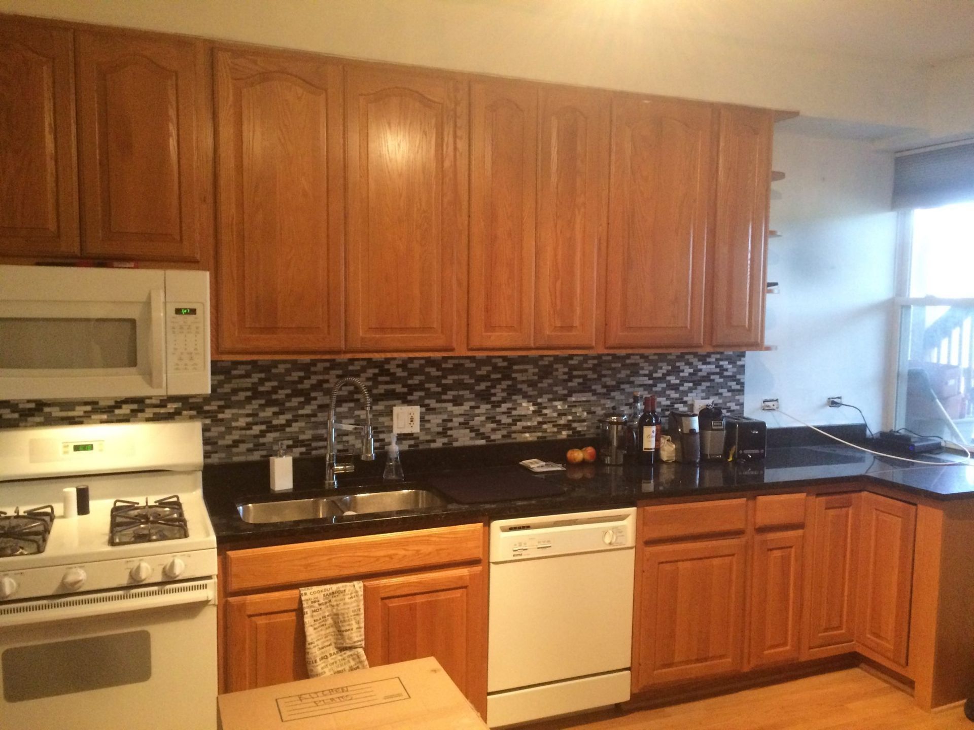 Kitchen interior with wood cabinets, black countertops, white appliances, and a mosaic tile backsplash.