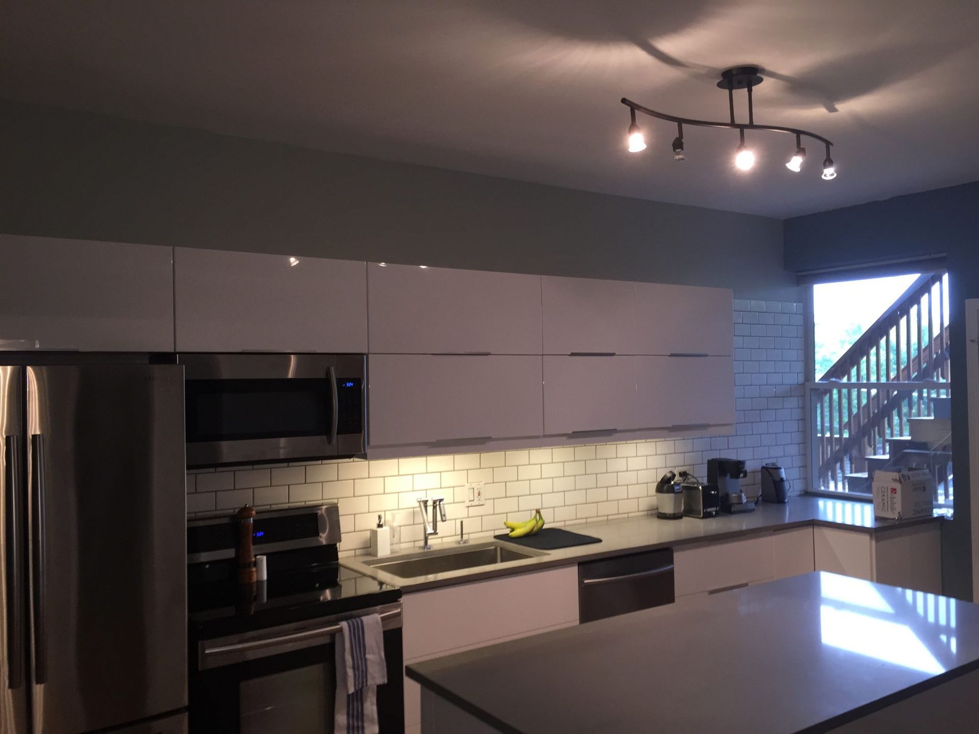 Modern kitchen with stainless appliances, glossy cabinets, tiled backsplash, and an island under ceiling lights