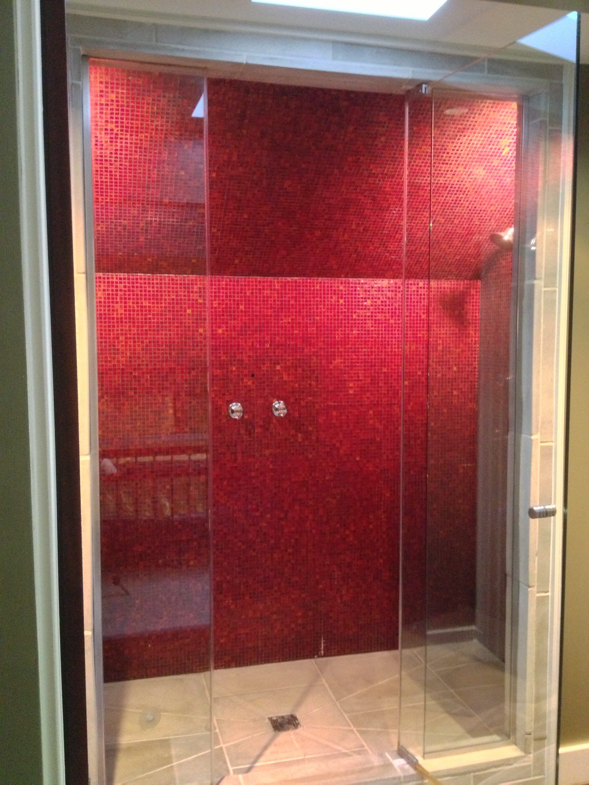 Red-tiled shower stall with glass doors and beige floor tiles.