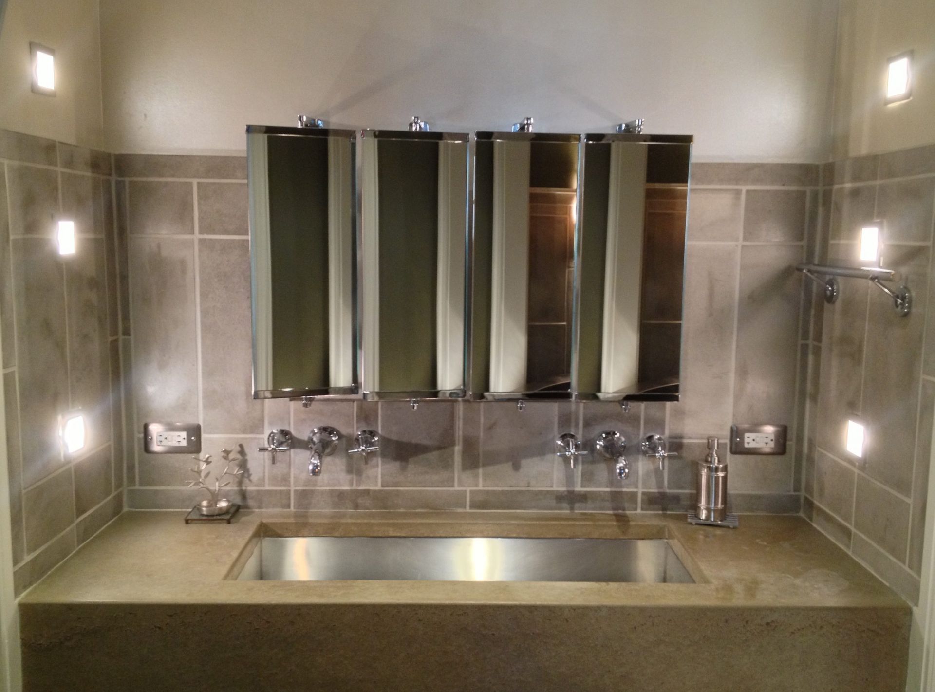 Modern public restroom sink with three mirrors and wall lights above a stainless-steel basin