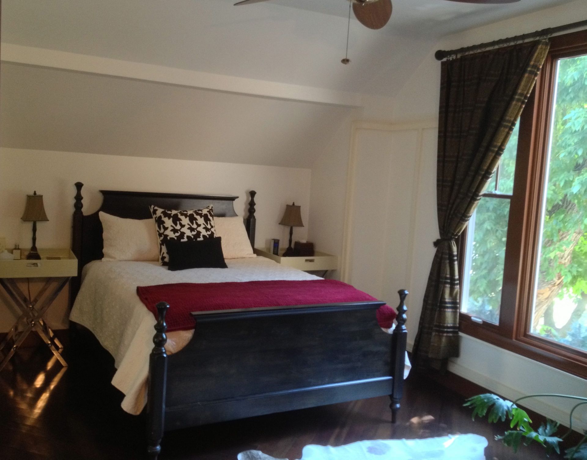 Bedroom with a dark wood bed, white bedding, red throw, and large window with curtains.